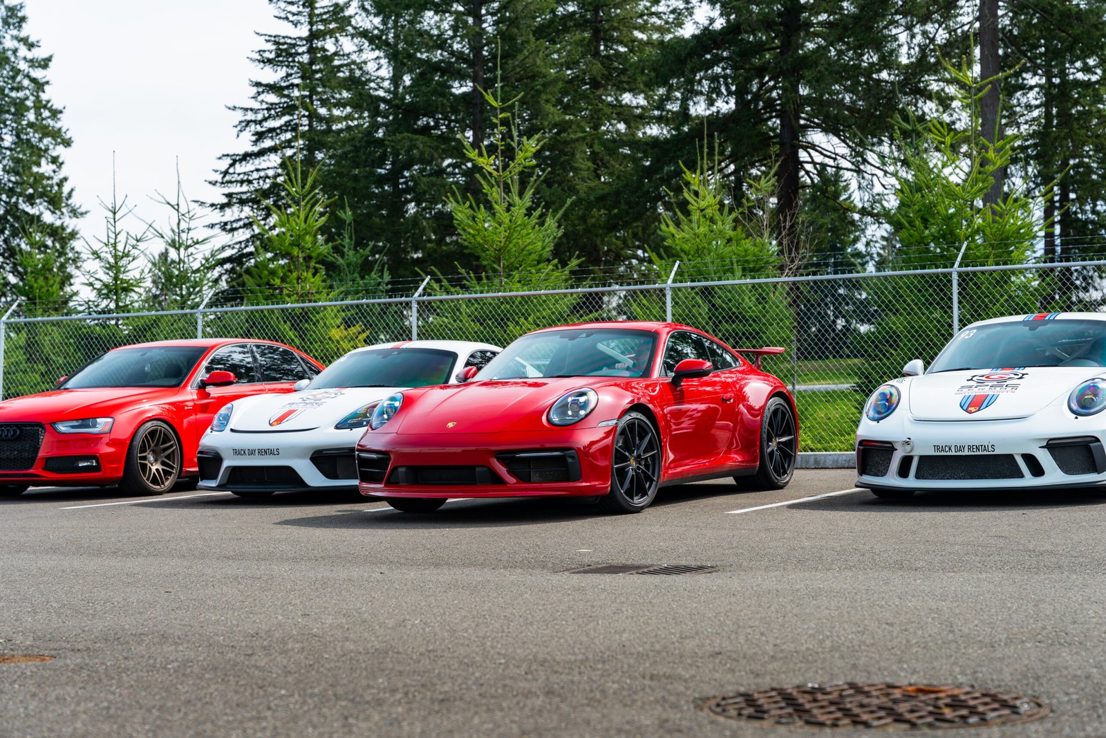 Red Porsche 911 and Sport Driving Motors track day rental cars lined up at a Washington racetrack paddock