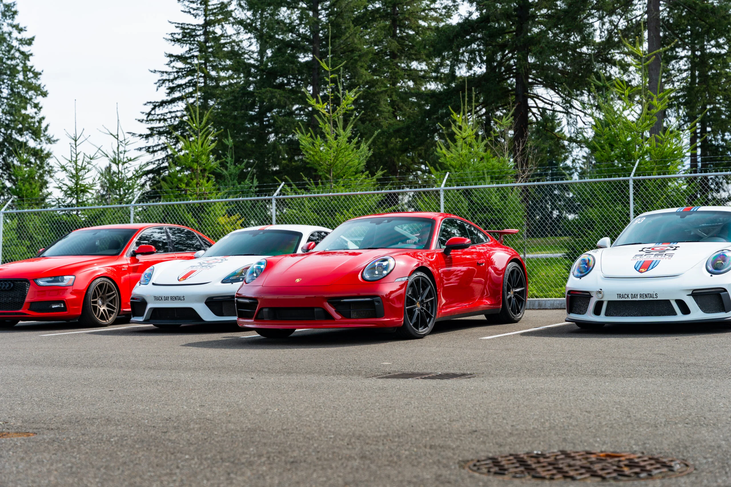 Red Porsche 911 and Sport Driving Motors track day rental cars lined up at a Washington racetrack paddock